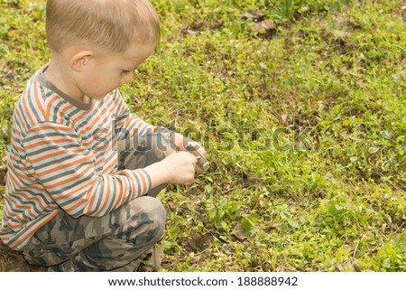 Young boy with a box of matches kneeling down in the green grass as he concentrates on trying to light a match to start a fire, with copyspace