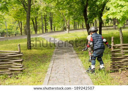 Two young boys in roller blades making their way carefully through the grass alongside an uneven cobbled stone path to reach a smoother road below