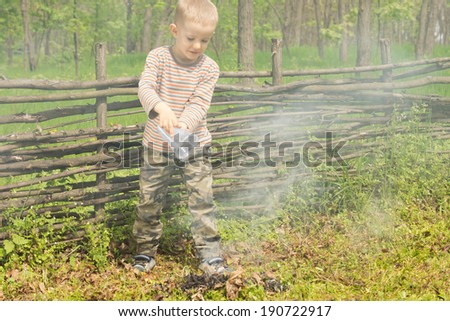 Little boy trying to extinguish a fire at a campsite pouring a container of water onto it resulting in a cloud of smoke
