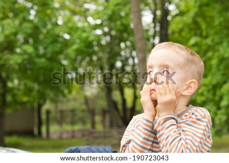 Little boy having fun pulling scary faces using his hands to pull down on his cheeks and distort his eyes, leafy green background with copyspace
