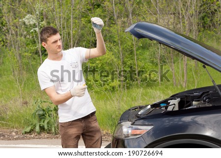 Mechanic checking the level of the oil on a car standing with the dipstick n his hand after the car broke down on a rural road
