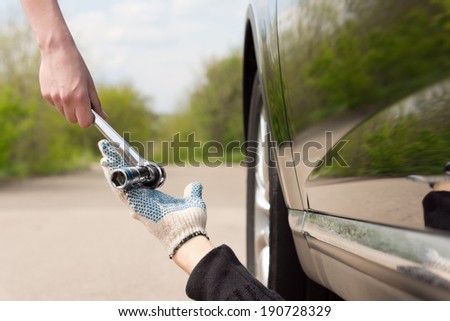 Woman handing a socket wrench or spanner to a mechanic working underneath her car after it has broken down at the side of a rural road