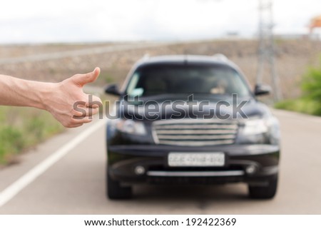 Close up of the hand of a young man standing thumbing a lift at the roadside trying to catch the attention of a female driver in an approaching car