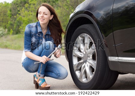 Smiling young woman getting ready to change a tyre crouching down at the side of the car holding a wheel spanner in her hands