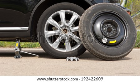 Fixing a puncture at the roadside with a view of the car jacked up with the spare tyre balanced against the side and nuts removed off the wheel