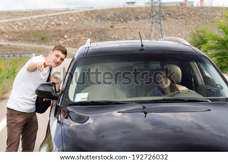 Female driver asking a handsome young for directions as he stands at the roadside pointing out the route for her on a rural road