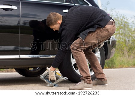 Man placing a hydraulic jack under his car to raise the vehicle allowing him to change the wheel for a spare following a roadside puncture