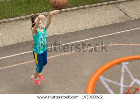 Active young teenage girl playing basketball leaping in the air as she throws the ball at the net, viewed from on top of the goalpost