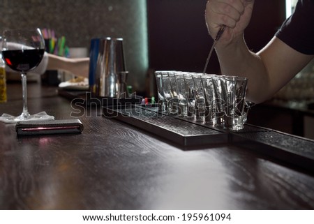 Row of glasses on a bar counter with the arm of a barman using a twizzle to mix alcohol inside one of them