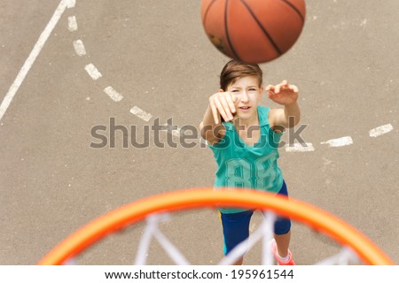 View from the top of the hoop of a young teenage girl practicing her basketball throwing the ball at the net trying for a goal