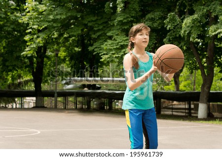 Beautiful teenage girl with her long brown hair in a plait playing basketball standing with the ball in her hands on an outdoor court