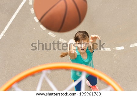 Attractive young teenage girl shooting a basketball at the hoop as she practises her aim and shooting a goal