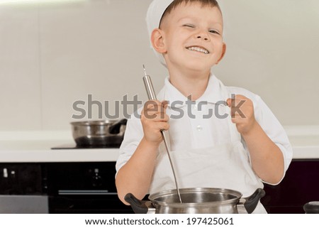 Happy young boy in a chefs toque enjoying cooking stirring the pot and cheering while punching the air with his other fist