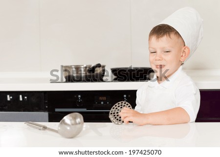Cute grinning little boy in a chefs hat and apron standing behind a kitchen counter with his utensils ready to start cooking