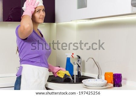 Housewife straightening her cap as she works in the kitchen washing the dishes in the sink