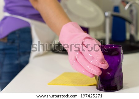 Woman placing a clean washed purple glass aside on the kitchen counter as she washes up the dishes in the sink