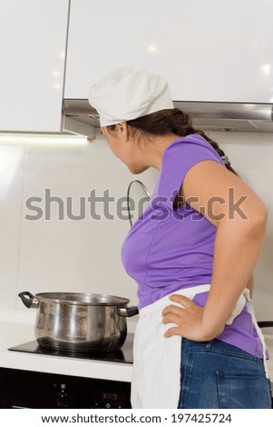 Woman chef watching her pot boil leaning over the hob to check on the contents as she prepares a meal