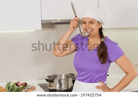 Happy friendly female chef standing smiling at the camera and tasting her food from a stainless steel ladle