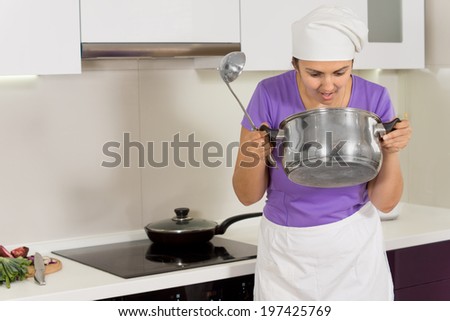 Cook in a white toque and apron standing alongside the hob checking the aroma of her food in the pot