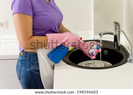 Woman wearing gloves washing dirty dishes in the kitchen sink