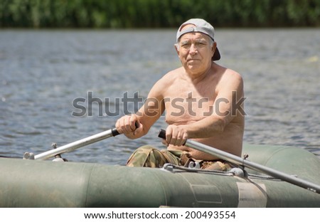 Smiling senior man enjoying a row in a rubber dinghy as he sits shirtless in the boat with his hands on the oars smiling at the camera