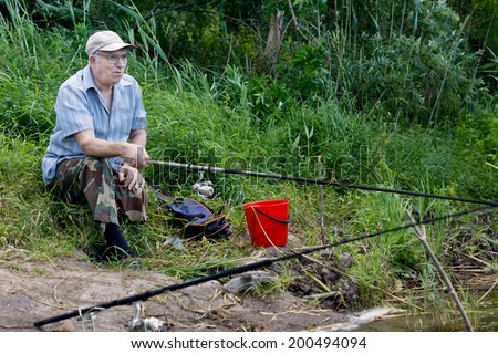 Elderly handicapped man with one leg enjoying a days fishing sitting on the shores of a freshwater lake with his rod and reel