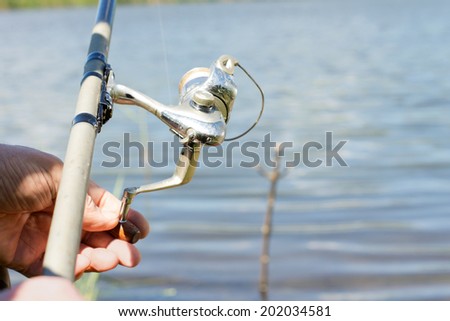 Fisherman using a spinning reel for freshwater fishing on a rural lake, close up of his hands and the reel