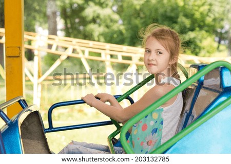 Smiling little girl sitting on a fairground ride gripping the colorful side bars as though not sure that she will enjoy the speed with an expression of trepidation