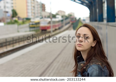 Beautiful young red haired woman with a sad facial expression waiting alone on the platform of a railway station