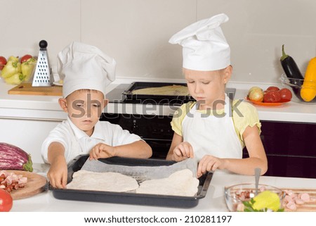 Little boy and girl in a chefs apron and toque making homemade pizza placing the rolled out pastry for the base onto a baking tray as they work as a team