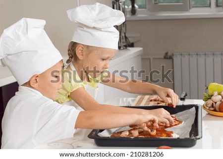 Young girl and boy in white chefs uniforms loading ingredients onto the homemade pizza bases they have just made before placing it in the oven
