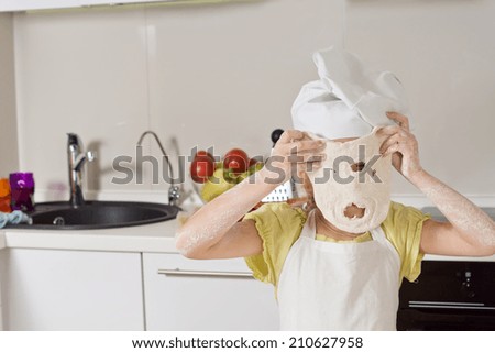 Little girl playing with a dough mask holding up a freshly rolled out portion of pastry through which she has punched a mouth and nose