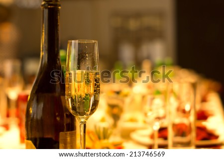 Elegant tall flute of chilled sparkling champagne standing alongside a full bottle on an elegant formal dining table at a catered event, party or reception