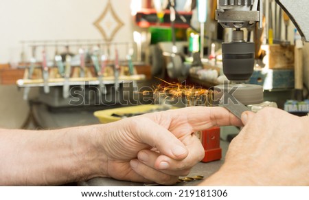 Hand of an elderly man sharpening a tool or filing a metal bar on a small electric bench grinder with flying sparks