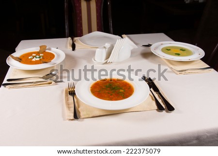 Table set with three different bowls of gourmet vegetable soup with artistic plating in white bowls for an appetizer to a formal dinner