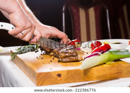 Close Up of Hand Chopping Meat with Knife on Cutting Board Amongst Other Vegetables