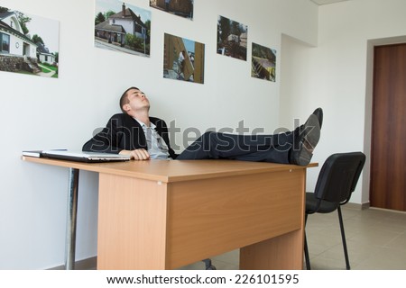 Young Businessman Taking Rest at the Office with Feet on the Wooden Table While Leaning on the Wall.