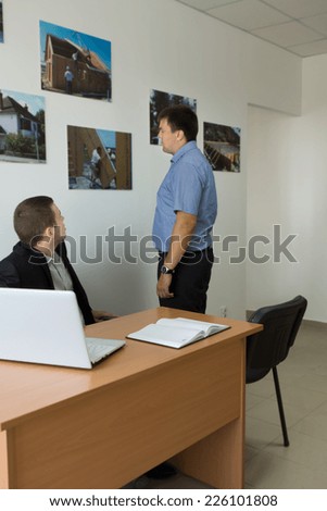 Middle Age Male Engineers Looking at Building Construction Photos Attached on Office Wall