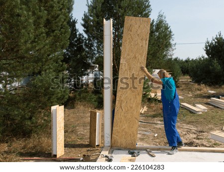 Worker in overalls standing erecting insulated wooden wall panels on a building site of a new house