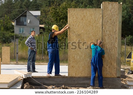Team of young builders erecting prefabricated wall panels on a building site of a new house