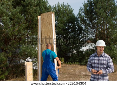 Construction workers busy erecting a corner insulated wooden wall panel and engineer on site working on a new house build