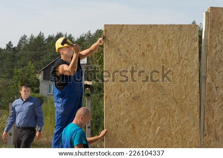 Construction workers erecting prefabricated walls of insulated timber positioning a panel for installation
