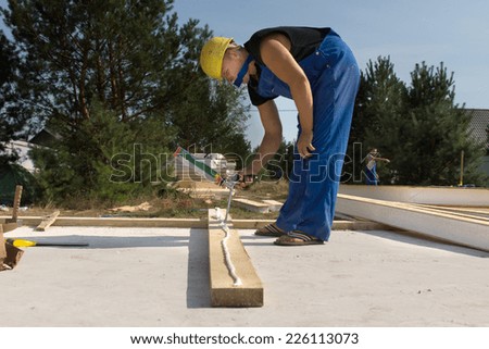 Builder or carpenter applying glue to a wooden beam on a construction site from a glue gun