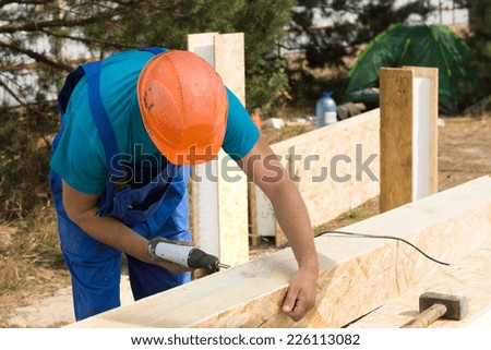 Workman drilling a hole in a wooden clad insulated beam on a new build construction site for a new house