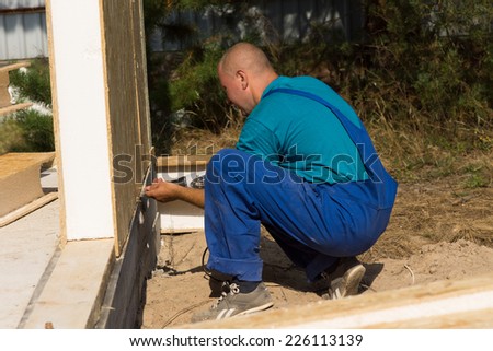 Workman installing insulated walls on a building site kneeling on the ground to align the bottom of the panel