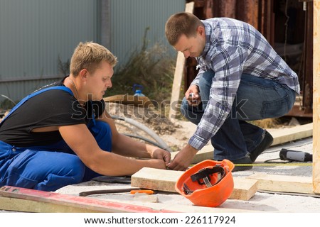 Two workmen working on a building site measuring insulation panels for installation at the corner of a new build house