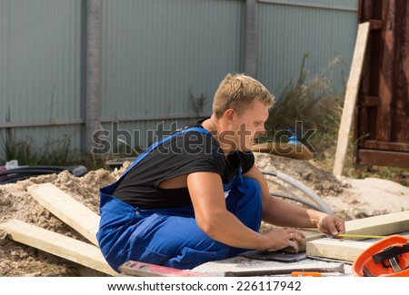 Workman on a building site taking a right angle measurement as he measure a wooden insulated beam before cutting and installing it