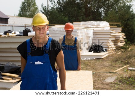Construction workers carrying insulated wooden wall panels on a building site approaching the camera
