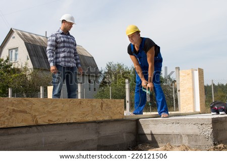 Male Building Engineer Looking at Construction Worker Busy Drilling a Wood at the Site.