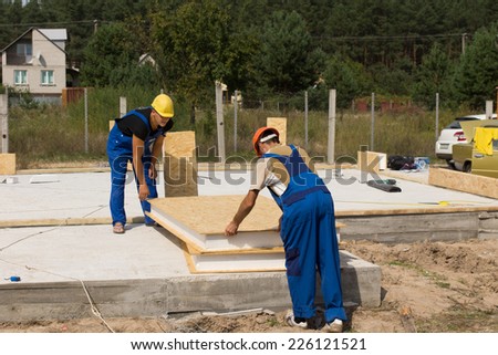 Two builders or construction workers handling insulated wall panels as they get ready to install them on the floor and foundation of a new build house